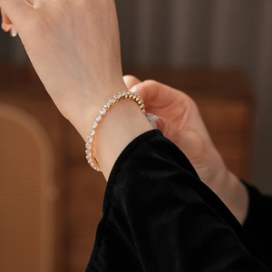 Close-up of a gold-finish tennis bracelet with round cubic zirconia on a model's wrist