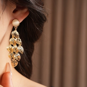 Close-up of gold hollow leaf tassel earrings with cat eye stones worn by a model