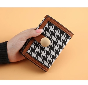 Detail of long houndstooth wallet with brown leather trim and golden snap button closure