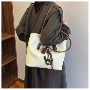 Detailed side view of cream white tote bag with brown straps and cute cat charms