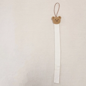 Close-up of a plush bear head charm on a white fabric hair accessory storage strap