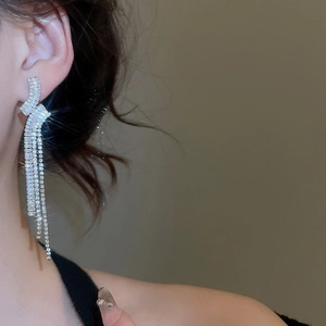 Dettaglio macro di lunghi orecchini a nappa in argento con zirconi indossati da una modella