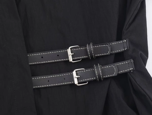 Close-up of black poplin shirt featuring leather straps with silver metal buckles