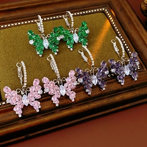 Detailed close-up of three pairs of zircon butterfly earrings in green, pink, and purple