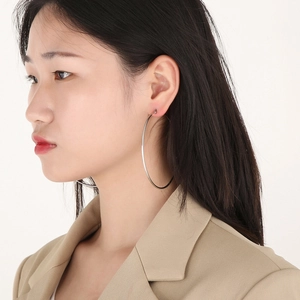 Close-up of a model wearing large silver stainless steel hoop earrings on a white background
