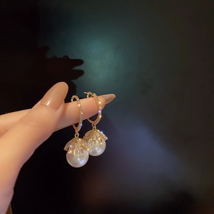 Close-up of gold hoop earrings with white pearls and sparkling zircon flower accents