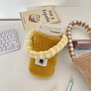 Vista macro de la funda de peluche amarillo para botella con bordado de gato negro