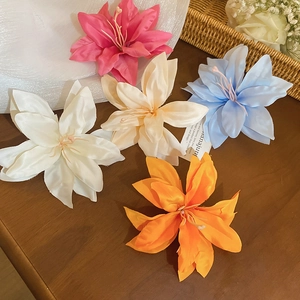 Detailed view of artificial fabric lily hair clips in five vibrant colors on a wooden table