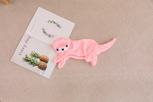 Flat lay of pink plush otter storage bag shell on a beige rug next to a magazine