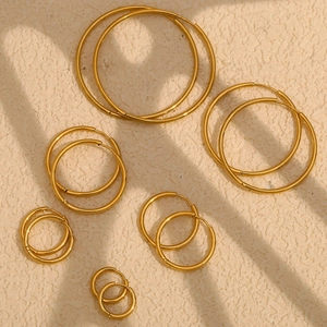 Macro view of various sized 18K gold plated stainless steel hoop earrings on beige texture