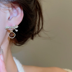 Close-up of golden bow earrings with diamonds and amber-colored round faceted gemstones