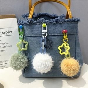 Close-up of plush pom-pom charms in three colors on a denim tote bag with star links