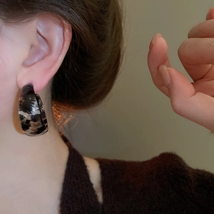 Close-up of leopard print resin C-shaped hoop earrings worn on a model's ear