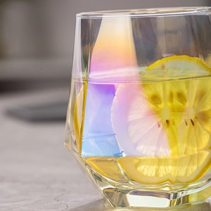 Close-up of hexagonal glass with rainbow coating, lemon slice, and yellow liquid