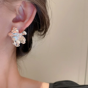 Detailed view of silver irregular liquid metal flower stud earrings on a model's ear
