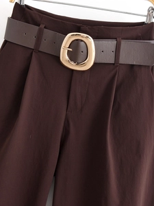 Dettaglio dei pantaloni larghi marrone scuro con cintura a fibbia ovale dorata