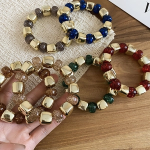 Detail of colorful acrylic beaded bracelets with gold square beads on a natural wood surface