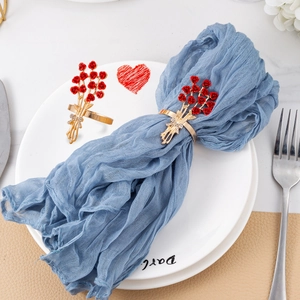 Detail of gold rose napkin rings with red crystal accents on a blue dinner napkin