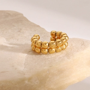 Macro detail of golden double-row beaded ear cuff resting on natural textured stone