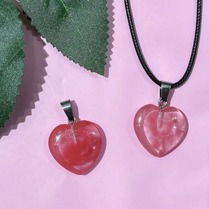 Close-up of heart-shaped pink crystal pendants and natural stone necklace on pink surface