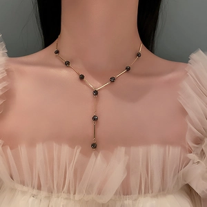 Elegant gold Y-shaped necklace with black faceted beads worn by a model over white gauze