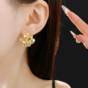 Close-up of golden floral stud earrings worn by a model against a black background