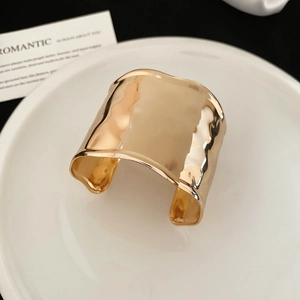 Detailed close-up of a wide gold cuff bracelet featuring a textured hammer finish