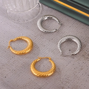Twisted geometric hoop earrings in gold and silver finish on a minimalist surface