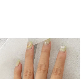 Close-up of almond-shaped nails with light yellow-green base, gold accents and pearls