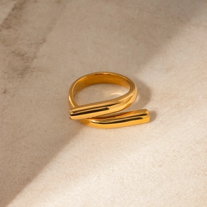 Detailed close-up of 18k gold-plated criss-cross ring with diamonds on beige stone