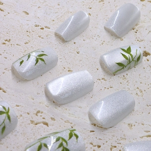 Cat eye press-on nails with shimmering bamboo leaf patterns on white stone surface