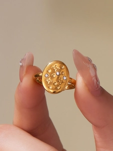 Macro detail of gold-plated oval ring featuring embossed star pattern and zircon stones