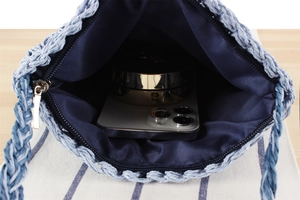 Detail view of woven beach bag interior with blue lining, zipper, phone, and powder box