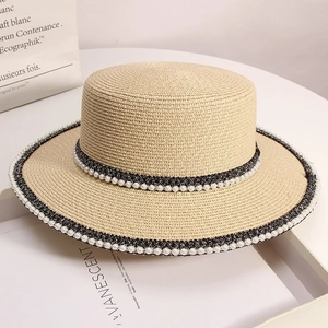 Detail of a beige straw boater hat featuring pearl embellishments and woven ribbon trim