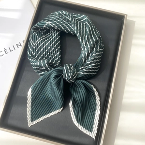 Detail of dark green pleated silk scarf with white stripes on a grey metal tray