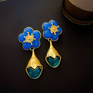 Close-up of royal blue floral earrings with golden accents and dark teal teardrop pendants