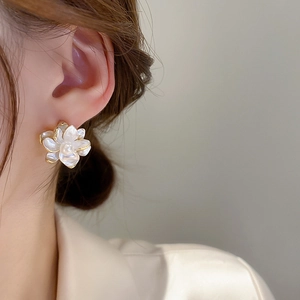 Detail of elegant floral pearl earrings with gold edges worn by a model in soft light