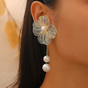 Detailed view of hollow gold flower earrings with pearls worn by a model in soft lighting
