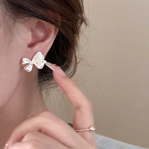 Elegant silver bow stud earrings with sparkling diamonds on a model's ear