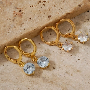 Elegant gold hoop earrings with sparkling zircon pendant on textured stone background