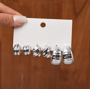 Detailed macro view of three pairs of silver C-shaped geometric metal hoop earrings