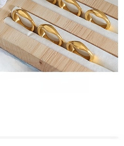 Detail of 6 polished gold-plated irregular wavy rings displayed on a white velvet stand