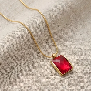 Detail of red rectangular gemstone pendant on golden snake chain over gray fabric