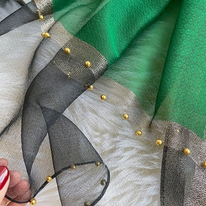 Close-up of silk scarf fabric showing green and black texture with gold bead trim