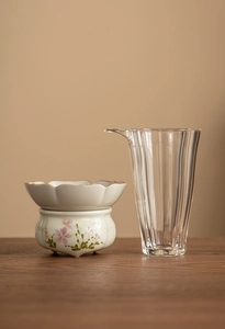 Detail of hand-painted ceramic tea strainer and textured glass cup on a plain background