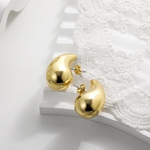 Macro shot of gold teardrop earrings with metal studs on white lace fabric