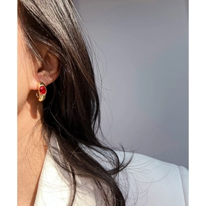 Close-up of elegant gold-plated C-shaped earrings with red emerald-cut zircon on a model