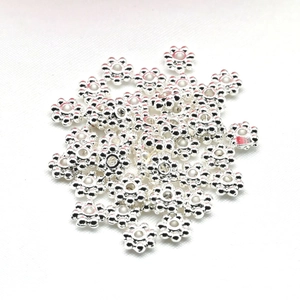 Shiny silver flower-shaped spacer beads for DIY jewelry making on white fabric