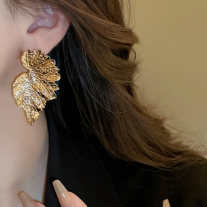 Detailed view of oversized gold leaf earrings with realistic vein texture on metal