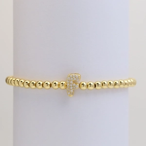 Detail of gold beaded stretch bracelet featuring a micro-pave zircon letter F charm